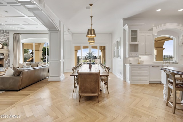 dining area with a fireplace, a wealth of natural light, light parquet flooring, and ornate columns