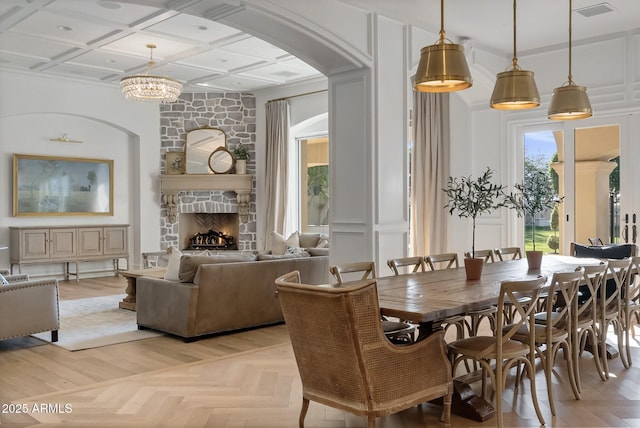 dining area featuring an inviting chandelier, light parquet flooring, coffered ceiling, and a stone fireplace