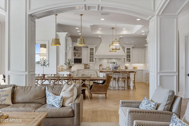 living room with ornamental molding, a tray ceiling, sink, and light parquet floors