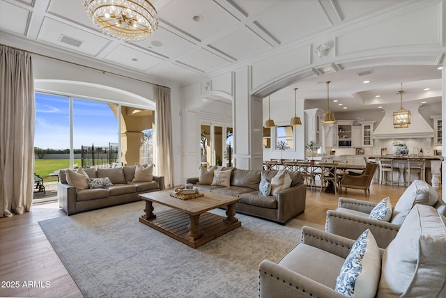 living room featuring coffered ceiling, light hardwood / wood-style flooring, and a notable chandelier