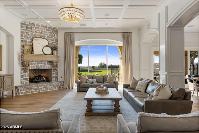 living room featuring a stone fireplace, coffered ceiling, a chandelier, and light hardwood / wood-style floors