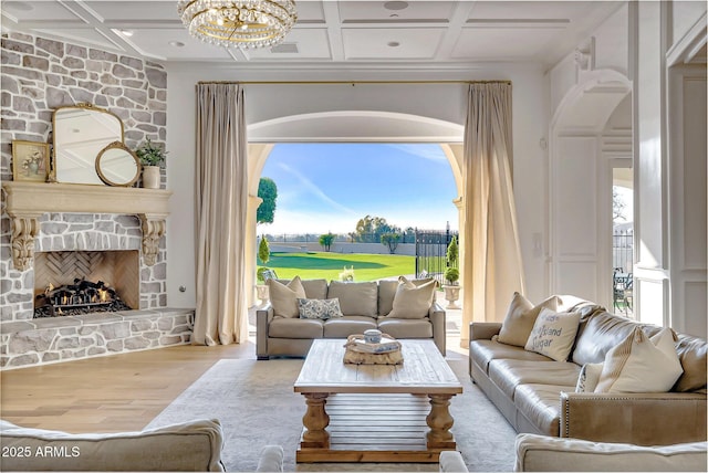 living room featuring coffered ceiling, a stone fireplace, plenty of natural light, and light hardwood / wood-style floors