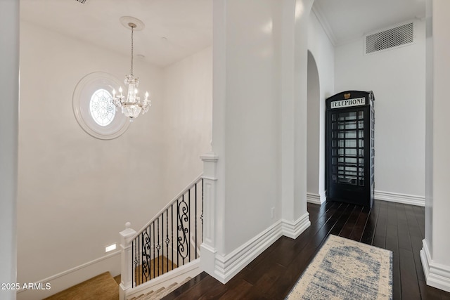 corridor featuring dark wood-type flooring, ornamental molding, and an inviting chandelier