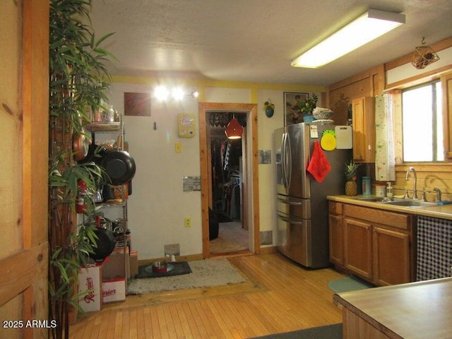 kitchen featuring stainless steel fridge with ice dispenser, light countertops, light wood-type flooring, brown cabinetry, and a sink