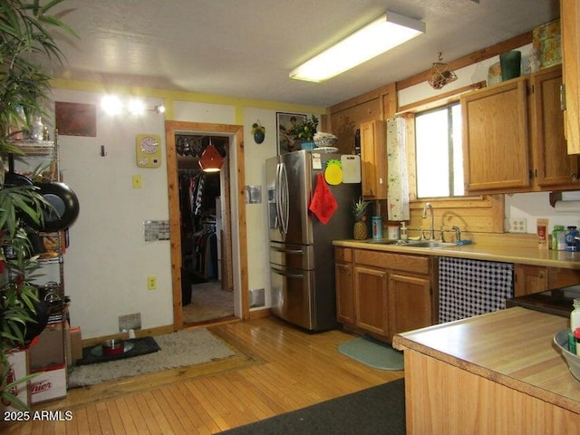 kitchen featuring brown cabinetry, light wood-style flooring, a sink, light countertops, and stainless steel refrigerator with ice dispenser