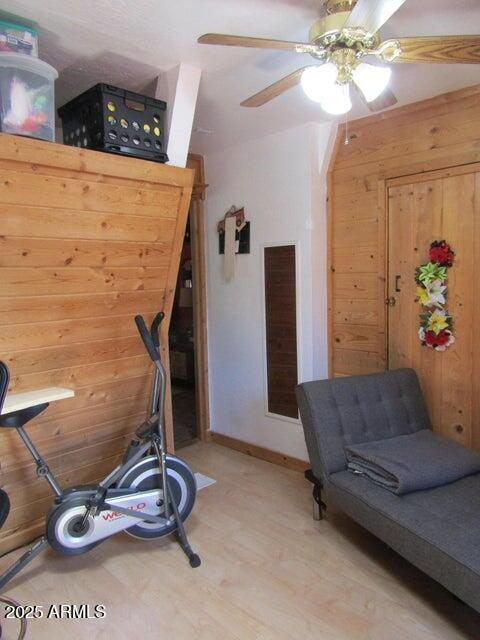 exercise room featuring light wood-type flooring, wooden walls, and ceiling fan