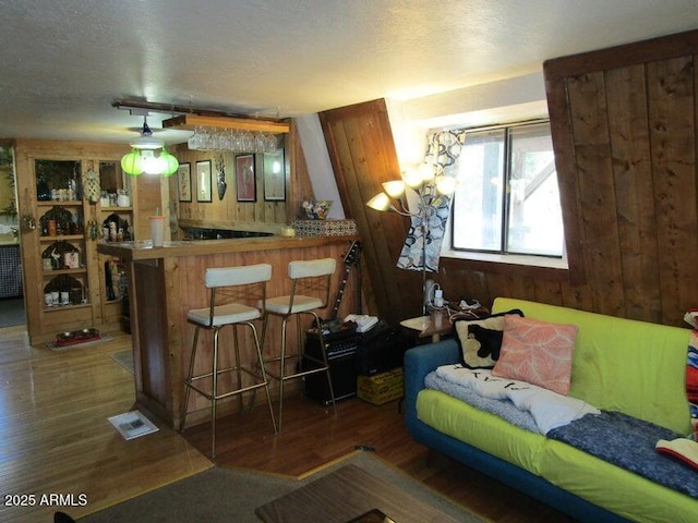 living room featuring wooden walls, wood finished floors, visible vents, bar, and a textured ceiling