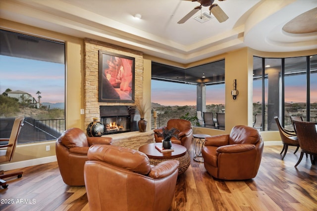 living room with ceiling fan, a fireplace, a raised ceiling, and hardwood / wood-style floors