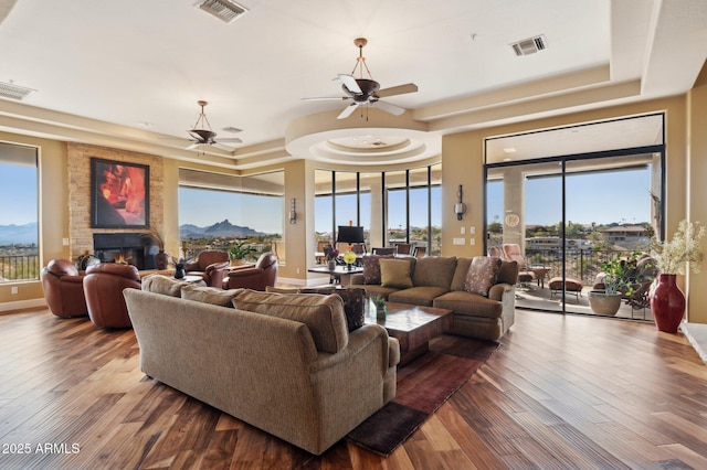 living room featuring hardwood / wood-style flooring, a fireplace, a raised ceiling, and ceiling fan