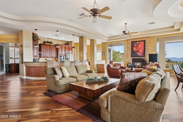 living room with a raised ceiling, ceiling fan, a large fireplace, and dark hardwood / wood-style flooring