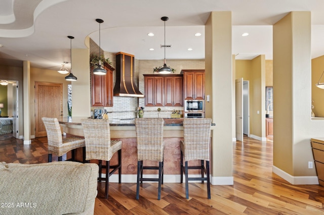 kitchen featuring built in microwave, decorative light fixtures, kitchen peninsula, and wall chimney exhaust hood