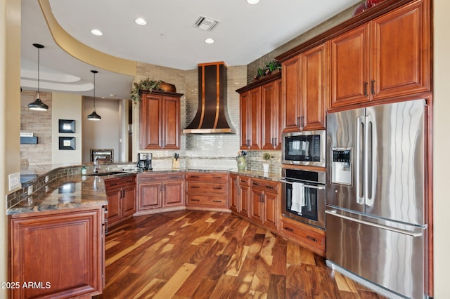 kitchen with stone countertops, hanging light fixtures, kitchen peninsula, stainless steel appliances, and wall chimney range hood