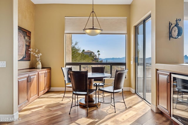 dining space with a mountain view, plenty of natural light, beverage cooler, and light wood-type flooring