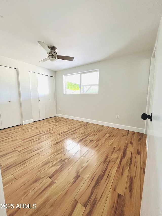 unfurnished bedroom featuring light wood-style flooring, baseboards, ceiling fan, and two closets