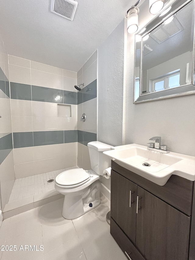 bathroom with a textured ceiling, toilet, vanity, visible vents, and tiled shower