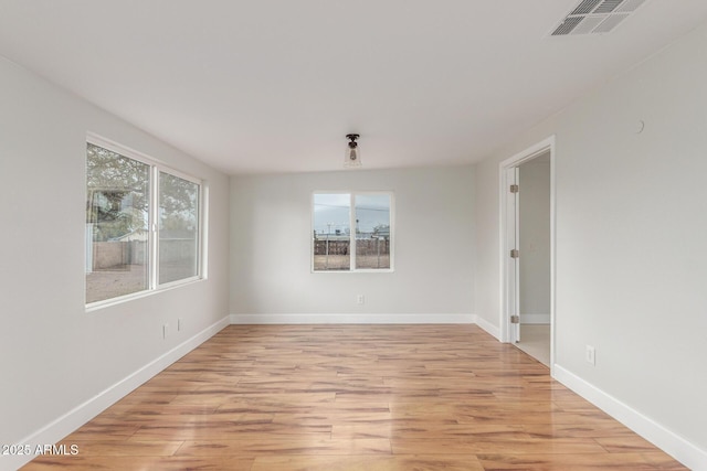 spare room with light wood-type flooring, visible vents, and baseboards