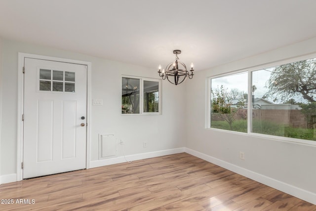 unfurnished dining area featuring light wood-style flooring, baseboards, and a notable chandelier