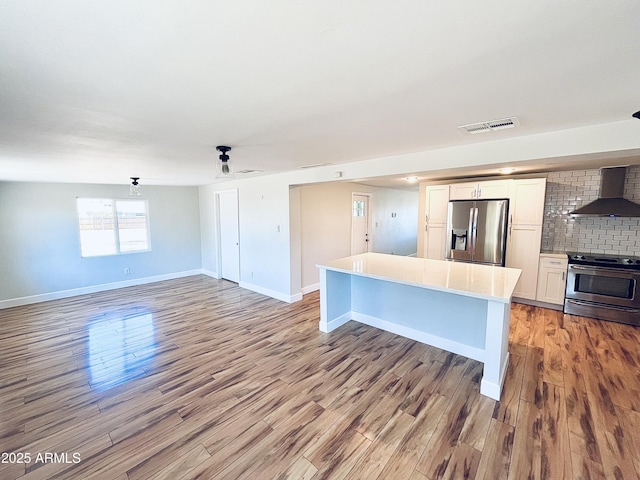 kitchen with light wood finished floors, tasteful backsplash, light countertops, appliances with stainless steel finishes, and wall chimney exhaust hood