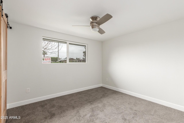 spare room with ceiling fan, a barn door, carpet, and baseboards