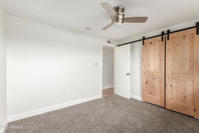 unfurnished bedroom with ceiling fan, a barn door, carpet flooring, and baseboards