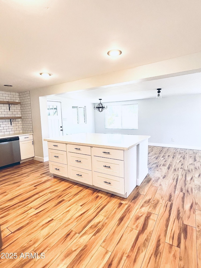 kitchen with light wood-style flooring, baseboards, white cabinets, light countertops, and stainless steel dishwasher