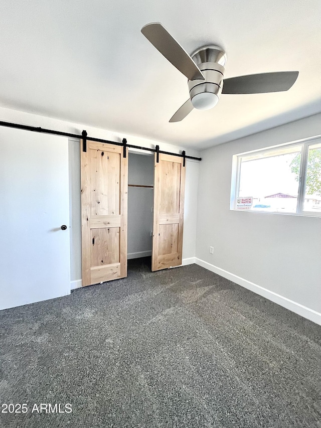 unfurnished bedroom featuring a ceiling fan, dark colored carpet, baseboards, and a barn door