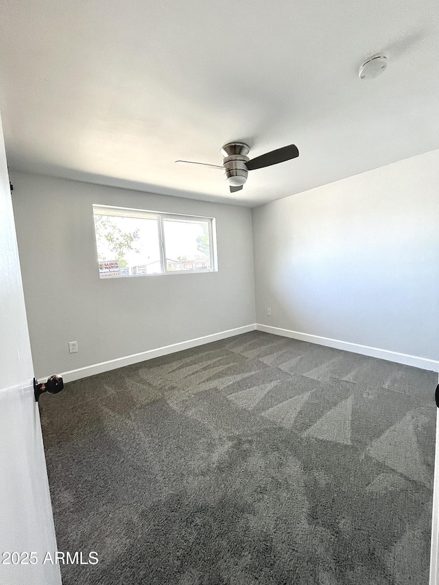 empty room featuring dark colored carpet, a ceiling fan, and baseboards