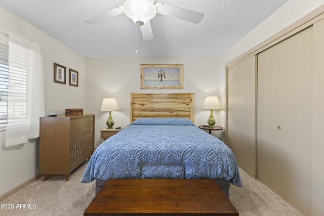 bedroom with light carpet, ceiling fan, a closet, and a textured ceiling