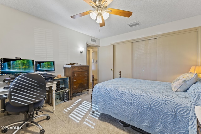 bedroom featuring ceiling fan, light colored carpet, a textured ceiling, and a closet