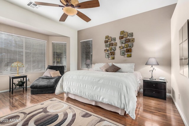 bedroom with ceiling fan, visible vents, baseboards, and wood finished floors