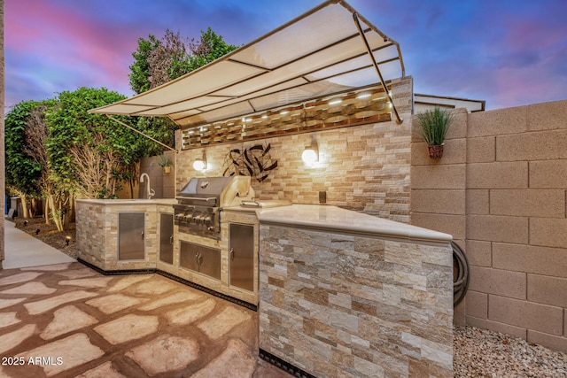 view of patio with area for grilling, a sink, exterior kitchen, and fence