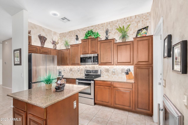 kitchen with light tile patterned floors, appliances with stainless steel finishes, brown cabinets, backsplash, and a center island