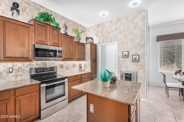 kitchen with brown cabinets, a kitchen island, appliances with stainless steel finishes, and light stone countertops