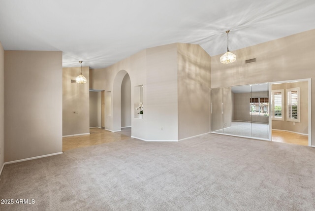 carpeted spare room with arched walkways, baseboards, a high ceiling, a notable chandelier, and visible vents