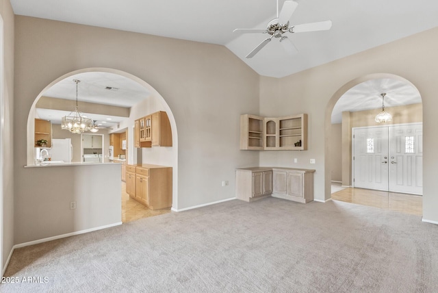 unfurnished living room featuring lofted ceiling, arched walkways, baseboards, light colored carpet, and ceiling fan with notable chandelier