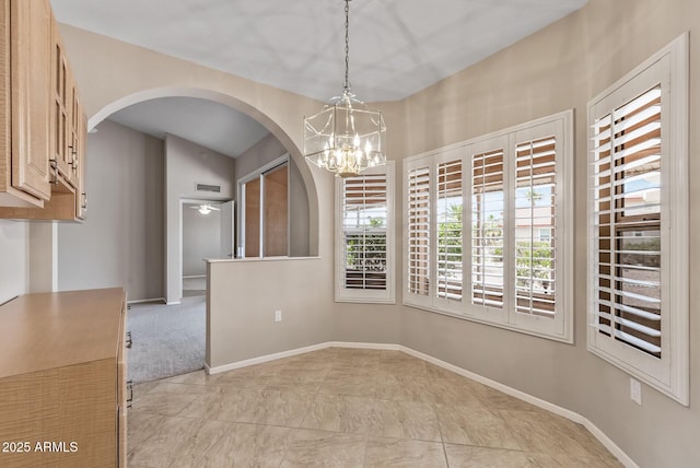 unfurnished dining area with arched walkways, an inviting chandelier, visible vents, and baseboards