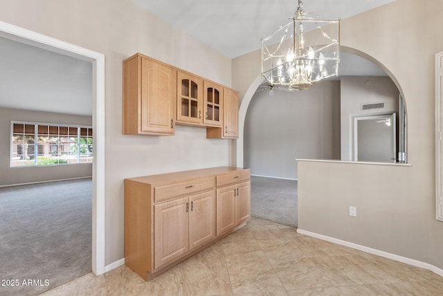 kitchen featuring light brown cabinets, arched walkways, an inviting chandelier, and light carpet
