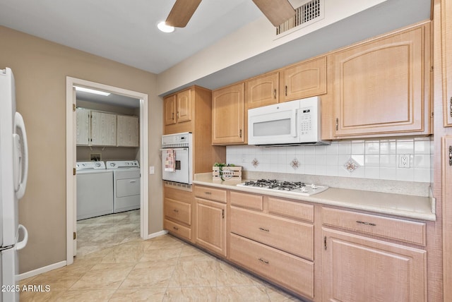 kitchen with light brown cabinetry, visible vents, baseboards, white appliances, and washer and dryer
