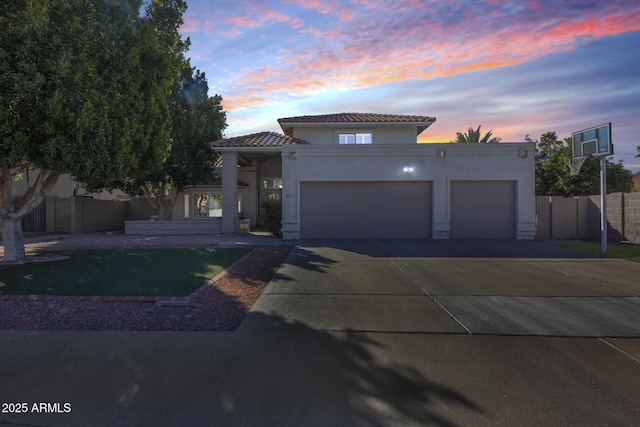 mediterranean / spanish-style house with an attached garage, fence, a tile roof, concrete driveway, and stucco siding