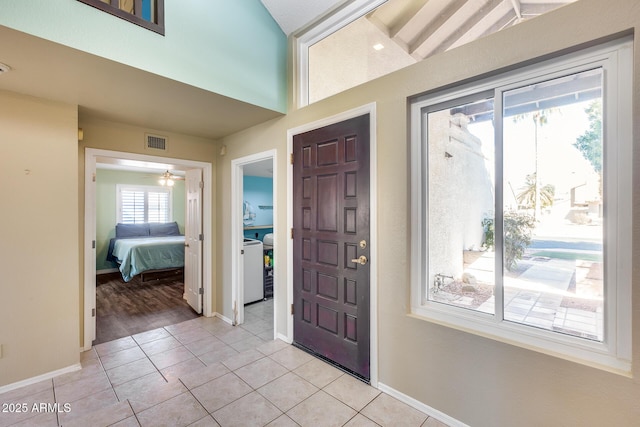 foyer entrance featuring light tile patterned floors, lofted ceiling, visible vents, and baseboards