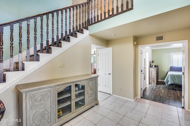 staircase with a towering ceiling, tile patterned flooring, visible vents, and baseboards