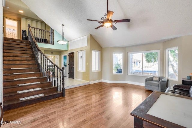 living room featuring stairway, a textured ceiling, wood finished floors, high vaulted ceiling, and baseboards