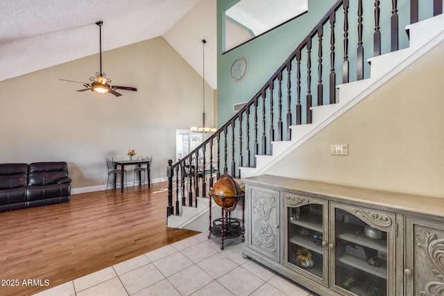 stairs with high vaulted ceiling, tile patterned flooring, baseboards, and ceiling fan with notable chandelier