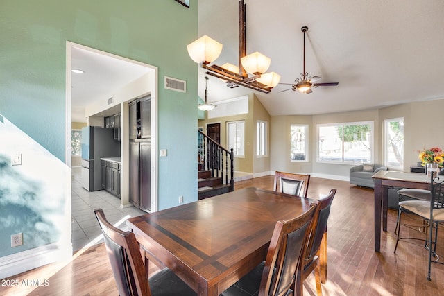 dining area with light wood-style floors, visible vents, stairway, and high vaulted ceiling