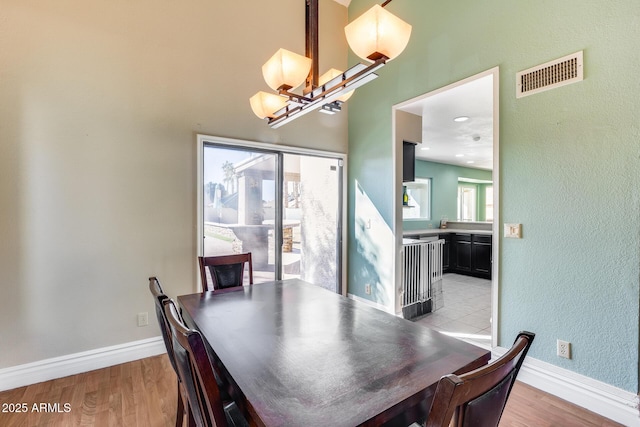 dining space featuring light wood finished floors, baseboards, visible vents, and a notable chandelier