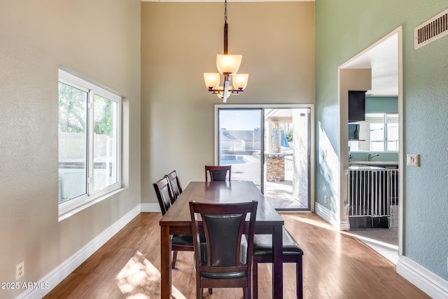 dining area featuring light wood-type flooring, a towering ceiling, visible vents, and baseboards