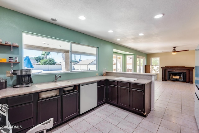 kitchen with a fireplace, light tile patterned floors, light countertops, a sink, and dishwasher