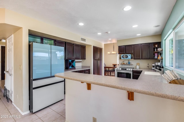 kitchen with a peninsula, a breakfast bar, light countertops, stainless steel electric range, and freestanding refrigerator