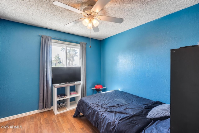 bedroom with a ceiling fan, a textured wall, a textured ceiling, and wood finished floors