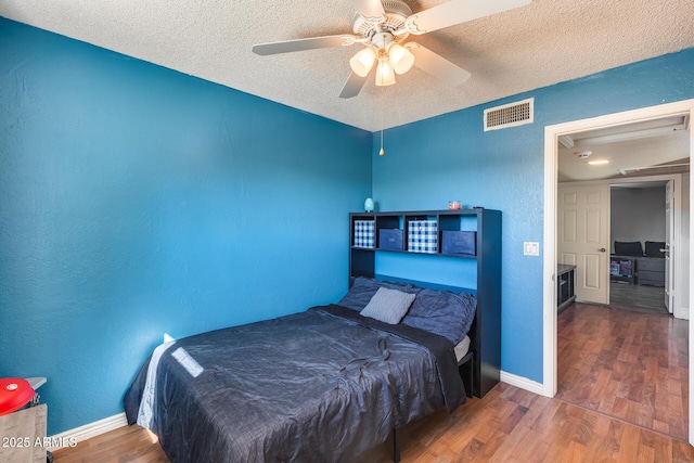 bedroom featuring a textured ceiling, a textured wall, dark wood-type flooring, and visible vents